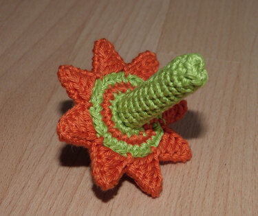 Gehäkelter Kreisel in Orange und Grün mit sternförmiger Basis auf Holzoberfläche.