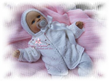 Weißes gestricktes Kapuzenjäckchen mit Schleife und passender Mütze auf rosa Decke
