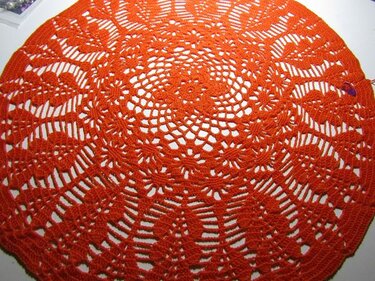 Rundes orangerotes Häkeldeckchen mit filigranem Blumen- und Spitzenmuster