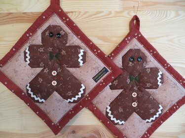 Zwei gequiltete Topflappen mit braunen Lebkuchenmann-Applikationen und rotem Sternchenrand