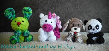 Vier gehäkelte Amigurumi-Tiere: grüner Hase, weißes Einhorn, brauner Hund und schwarz-weißer Panda auf flauschigem Untergrund.