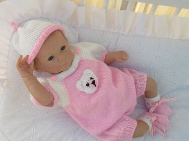 Babypuppe trägt ein rosa-weißes Baby-Strickset mit Bärenmotiv, Höschen, Mütze und Booties