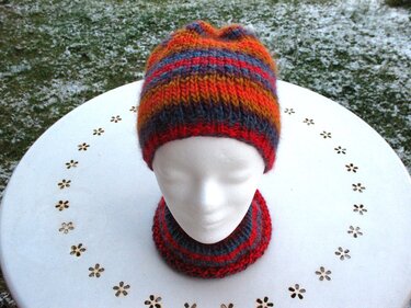 Bunte gestrickte Mütze und Loop auf weißem Schaufensterkopf vor leicht verschneitem Rasen