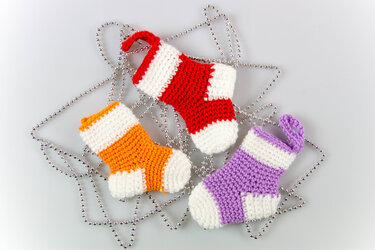 Drei gehäkelte Mini-Weihnachtsstrümpfe in Rot, Orange und Violett auf silberner Perlenkette