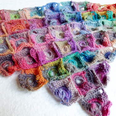 Nahaufnahme eines gehäkelten Dreieckstuchs aus bunten Granny-Squares mit zentralen Kreisformen.