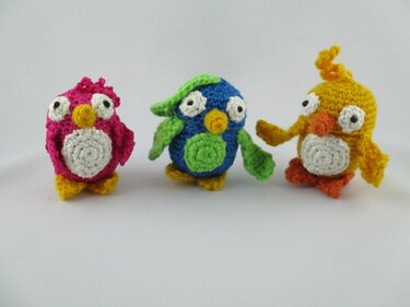 Drei bunte gehäkelte Amigurumi-Vögel (pink, blau, gelb) vor hellem Hintergrund