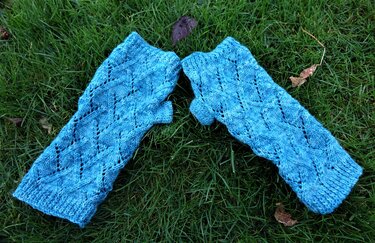 Zwei blaue fingerlose Armstulpen mit Rautenmuster auf grünem Gras