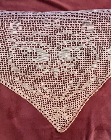 helles gehäkeltes Dreieckstuch im Filetmuster mit symmetrischem Tiermotiv auf dunklem Untergrund