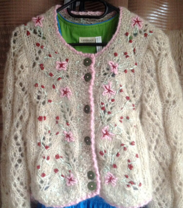 Cremefarbene Kurzstrickjacke mit Ajourmuster, rosa Blumenstickerei und dunklen Knöpfen
