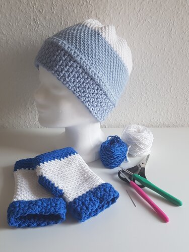 Gehäkelte Mütze und Stulpen in Blau-Weiß mit Garnknäueln, Häkelnadeln und Schere auf weißer Fläche