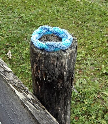 Braided blue knitted headband on a weathered wooden post with green grass in the background.