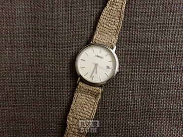 Armbanduhr mit beigem gehäkeltem Uhrenband auf dunkelgrauem Stoff