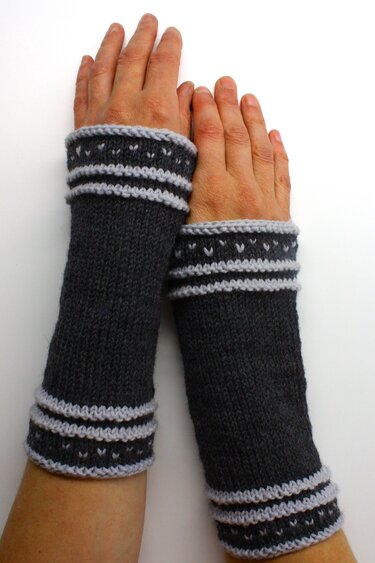 Gestrickte dunkelgraue Armstulpen mit hellgrauen Bündchen und Punkt- und Streifenmuster an Händen
