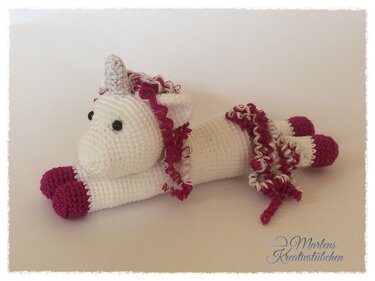 Gehäkeltes weißes Amigurumi‑Einhorn mit pinken Hufen und lockiger Mähne, seitliche Ansicht