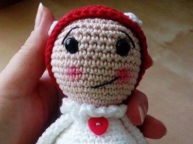 Gehäkelte Puppe in Rot und Weiß mit herzförmigem Knopf und lächelndem Gesicht, Nahaufnahme