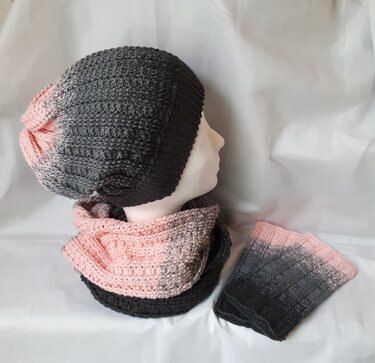 Gehäkeltes Set mit Slouch‑Mütze auf Schaufensterkopf, Loop und fingerlosen Armstulpen in Grau‑Rosa