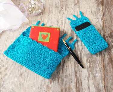 Gehäkeltes Set aus türkiser Buchhülle und Handytasche mit Zickzack-Muster auf Holz