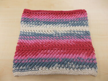 Gefalteter gestrickter Loop mit diagonalen Streifen in Rot, Rosa, Grau und Creme auf hellem Holz