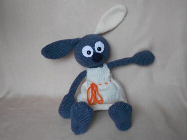Gehäkelter blaugrauer Amigurumi-Hase mit weißem Kleid und oranger Schnürung, sitzend
