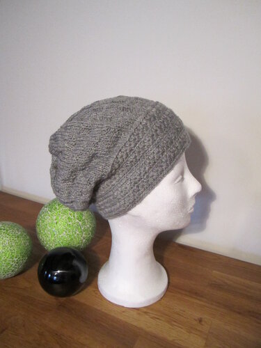 Schaufensterkopf mit grauer, gestrickter Slouch‑Mütze und Rippenbündchen; Dekokugeln auf Holzfläche