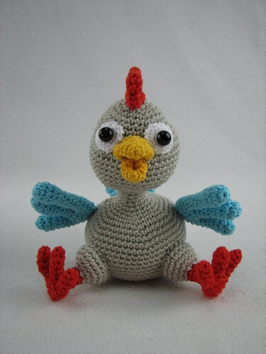 Gehäkeltes Amigurumi‑Huhn grau mit rotem Kamm, gelbem Schnabel und blauen Flügeln