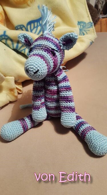 Gehäkeltes gestreiftes Amigurumi-Zebra in Pastellblau und Lila, sitzend