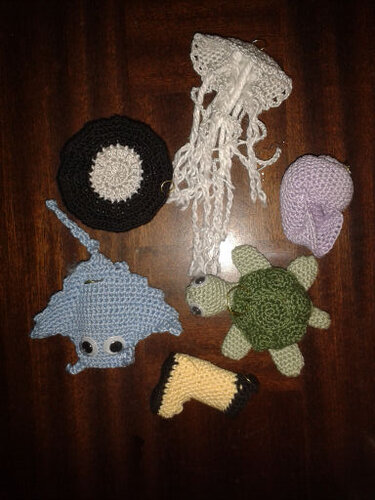 Gehäkelte Meerestiere und Kinderspielzeuge (Qualle, Rochen, Schildkröte, Schnecke) auf dunklem Holztisch