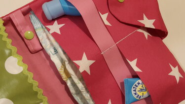 Offene Stoff-Wickeltasche in Magenta mit weißen Sternen und grünen Details, mit Fächern und Babyartikeln