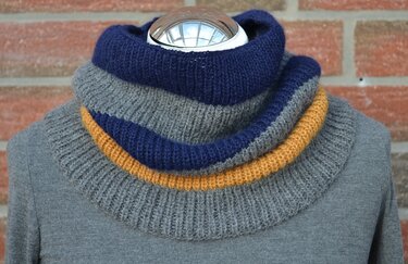 Gestrickter Loop-Schal mit blauen, grauen und senfgelben Streifen auf einer Schaufensterpuppe