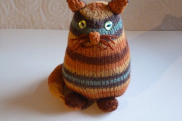 Gestrickte Amigurumi-Katze mit bunten Streifen und grünen Augen