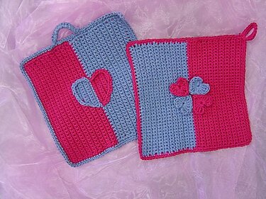 Zwei quadratische gehäkelte Topflappen in Pink und Hellblau mit Herzapplikationen und Aufhängeschlaufen