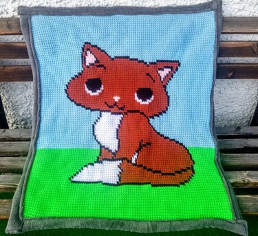 Handgehäkelte Babydecke mit sitzendem Fuchs auf blau-grünem Grund