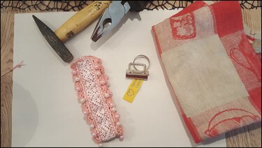 Gehäkeltes Band mit Perlen und Metallklemme neben Zange und Hammer als DIY-Setup