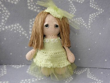 Amigurumi-Puppe im hellgrünen Häkelkleid mit Tüllrock, braunen Garnhaaren und Schleife vor grauem Sternenstoff.