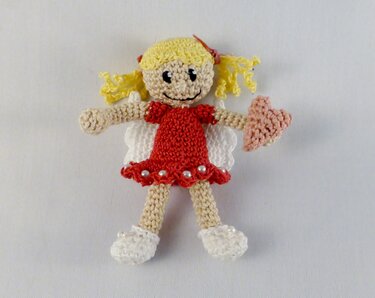 Zierliche gehäkelte Engel-Puppe mit gelbem Haar, rotem Kleid, weißen Flügeln und rosafarbenem Herz