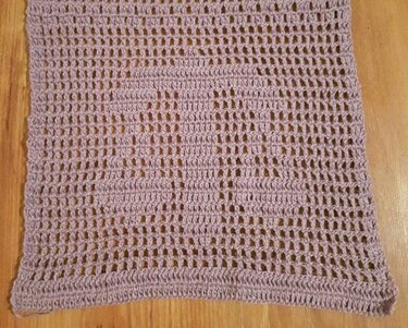 Gehäkeltes Tuch in hellem Lavendel mit Lochmuster auf Holzuntergrund