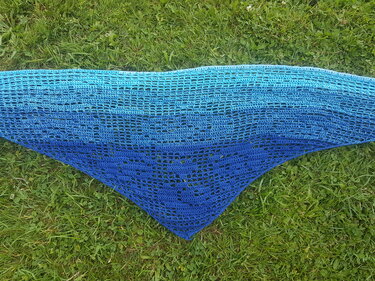Gehäkeltes dreieckiges Tuch mit Netzmuster und Motiv, Farbverlauf von Türkis zu Blau, ausgebreitet auf Gras