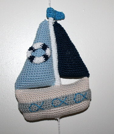 Gehäkeltes Segelboot mit hell- und dunkelblauen Segeln, beigem Rumpf, besticktem Band und kleinem Rettungsring