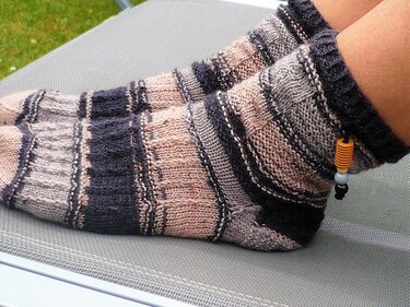 Handgestrickte Damensocken mit Streifen in Grau, Rosé und Anthrazit und Perle am Bündchen, getragen an Füßen