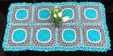Rechteckiger gehäkelter Tischläufer aus acht Granny-Squares in Türkis, Grau und Weiß mit zackiger Kante und Glasvase mittig