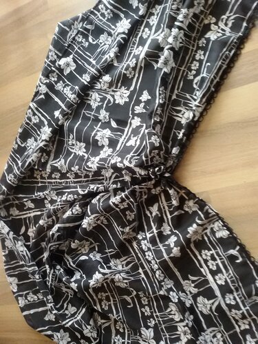 Schwarze Damenjacke mit weißem Blumen- und Linienmuster, Bindeband und Saumborte auf hellem Boden