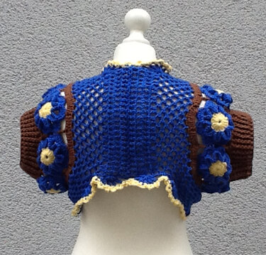 Gehäkelter Kurz-Bolero, Rückansicht auf Schneiderpuppe: offenes Netzrücken, braune Ärmel mit blauen Häkelblumen und gelbem Saum