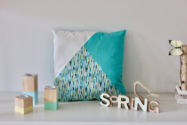 DIY-Kissenbezug mit Dreiecksblock in Türkis, Weiß und gemustertem Stoff auf Sideboard mit pastellfarbenen Holzkerzenhaltern