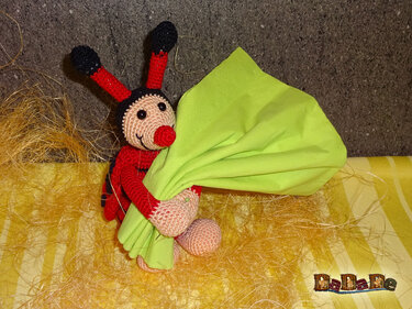 Gehäkelter Marienkäfer in Rot und Schwarz hält ein hellgrünes Tuch.