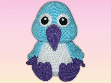 Gehäkelter Amigurumi-Vogel mit blauem Kopf, weißem Bauch und lila Schnabel und Füßen.