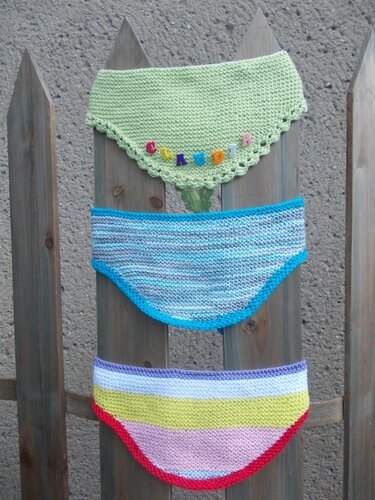 Drei gestrickte Dreieckshalstücher in Pastellgrün, Blau und gestreift an einem Holzzaun