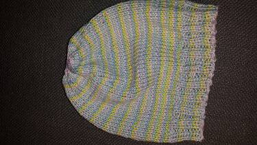 Gestrickte Babymütze in melierten Pastellfarben (Blau, Gelb, Rosa) auf dunklem Hintergrund