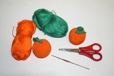Zwei gehäkelte Orangen, orange und grüne Garnknäuel, Schere und Häkelnadel auf weißem Hintergrund