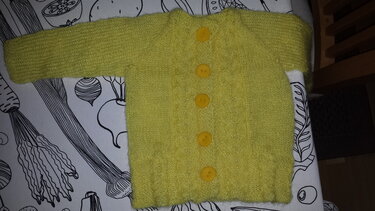 Gelbe gestrickte Babyjacke mit fünf Knöpfen auf gemustertem Untergrund
