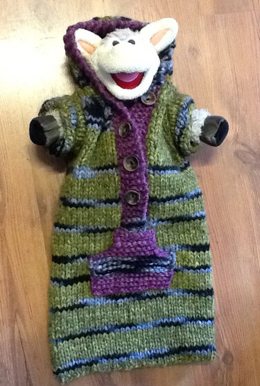 Gestrickter Babyschlafsack mit Kapuze, gestreift in Grün, Lila und Blau; Stofftierkopf schaut hervor